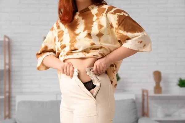 Image of woman trying to do her trousers up after pregnancy weight gain Peterborough